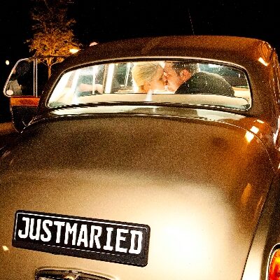Rear view of a vintage car at night with a “Just Married” sign, showing the bride and groom kissing inside.