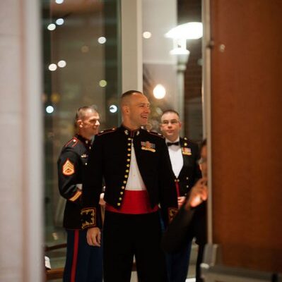 Three men in formal military dress uniforms standing indoors near a doorway during an event.
