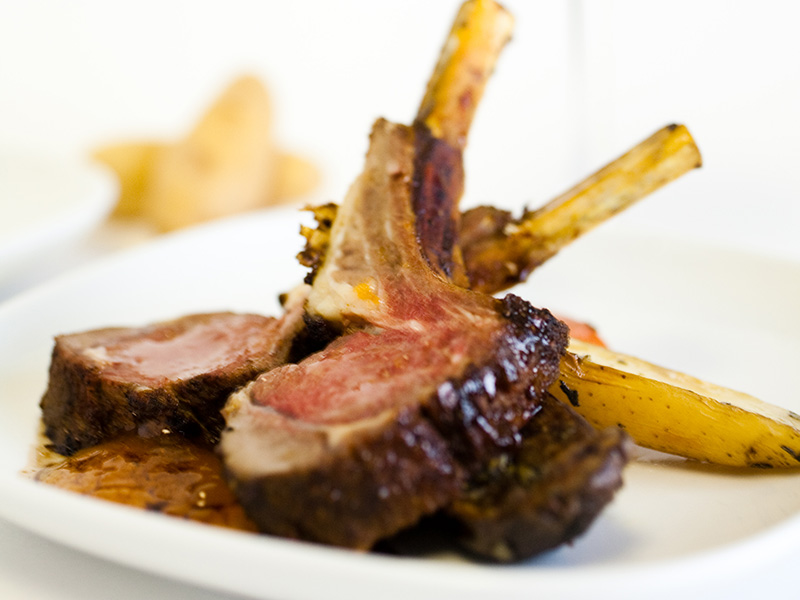 Plated rack of lamb with sliced chops, roasted vegetables, and sauce