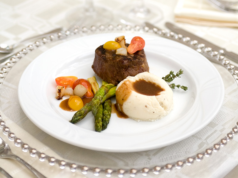 Plated filet entrée with mashed potatoes, asparagus, roasted tomatoes, and sauce