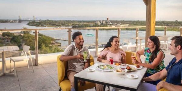 1 website where to eat Four people enjoying drinks and a meal on an outdoor terrace overlooking a river and distant waterfront skyline.
