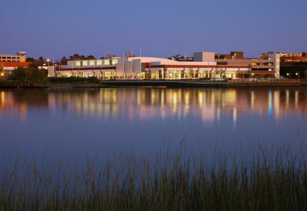 Twilight view of a waterfront convention center with building lights reflecting across calm water and marsh grass in the foreground.