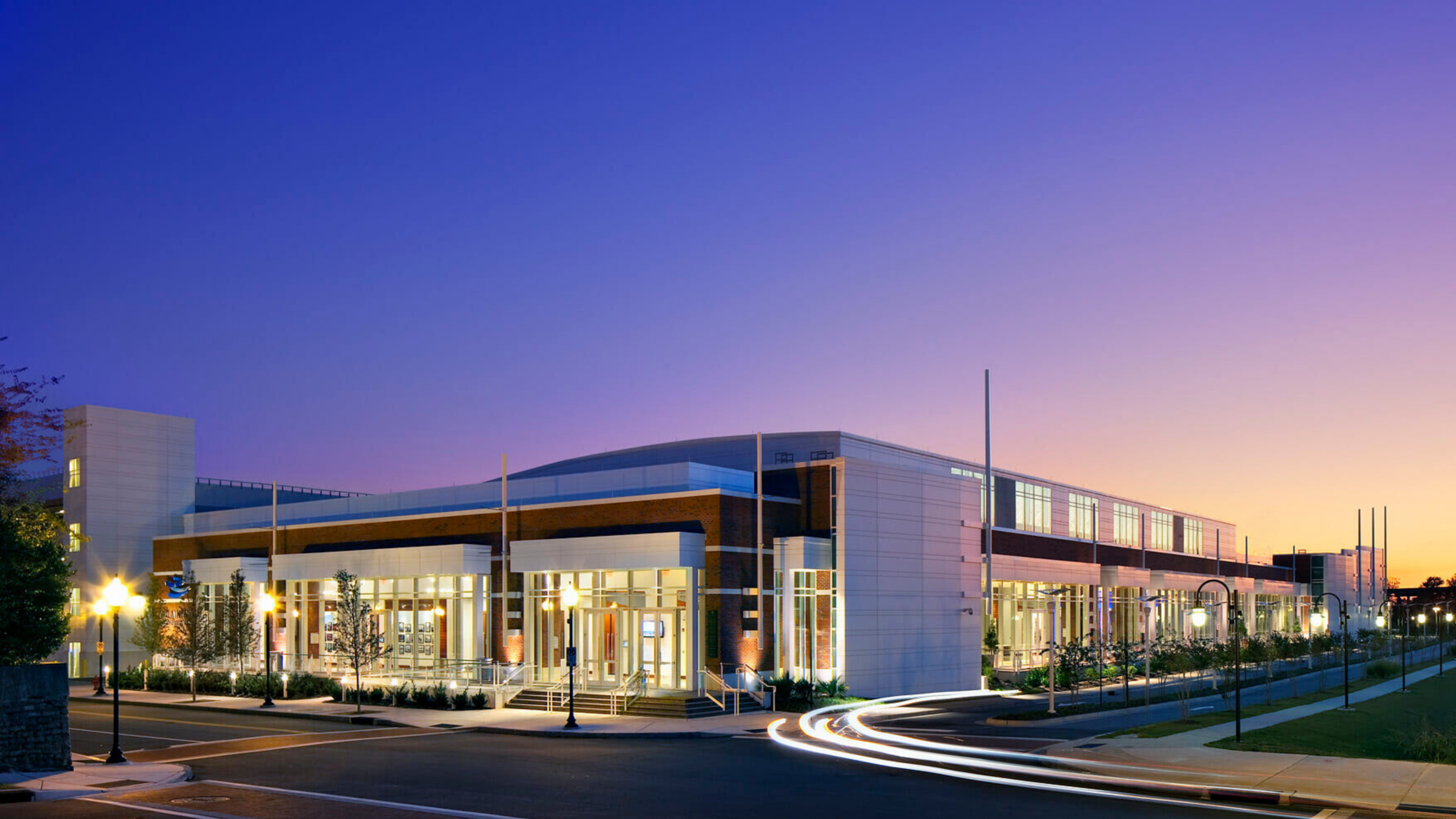 Twilight exterior view of the Wilmington Convention Center with illuminated glass entrances and windows beneath a purple-and-gold sunset sky.