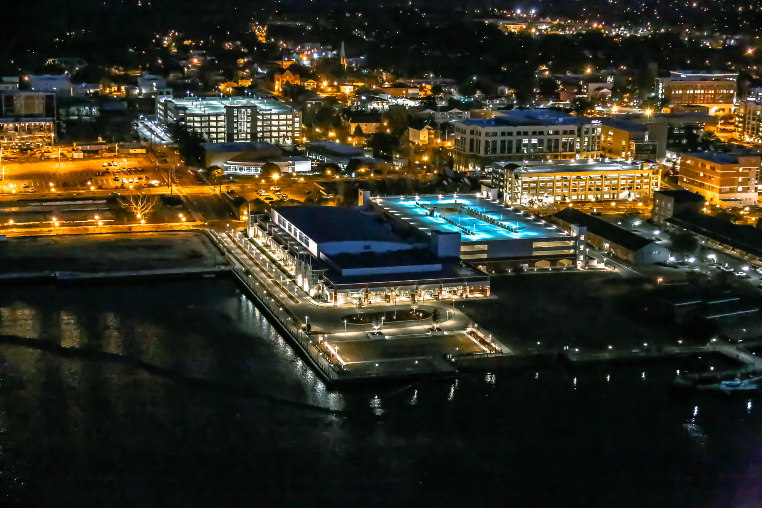 Aerial nighttime view of the Wilmington Convention Center and surrounding downtown waterfront, with illuminated streets, buildings, and parking deck lights reflecting along the river.